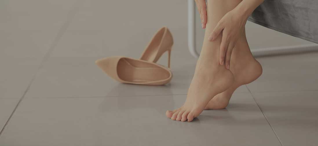 Barefoot woman rubbing her ankles next to discarded high heels.